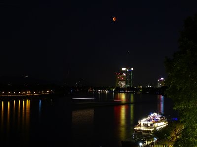 Abb. 10: Mond und Mars über dem DHL-Tower; die rötliche Strichspur links der Mitte stammt von einer Drohne; auf dem Rhein ein zur Strichspur &quot;gewarptes&quot; Schiff (23:01 MESZ).