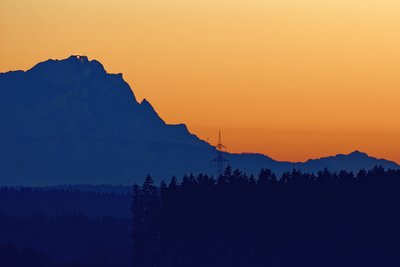 Zugspitze von Ebersberg aus. Luftlinie ca. 107 km. Gut erkennbar der Mast der Ehrwalder Zugspitzseilbahn (neben Strommast) sowie das Seil.