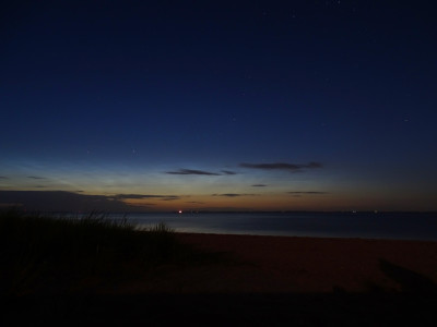 Leuchtende Nachtwolken über Föhr, aufgenommen in Steenodde/Amrum am 12.06.2022 um 01:21 MESZ. Dies entspricht fast auf die Minute der astronomischen Mitternacht - dunkler wird es im äußersten Norden Deutschlands um diese Jahreszeit nicht. Die Sonnendepression betrug -12.2°, sodass die astronomische Dämmerung formal so gerade noch erreicht wurde.